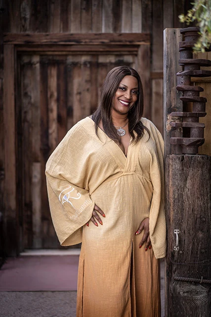 Marvina Thomas in a flowing gold dress in front of a rustic wooden door
